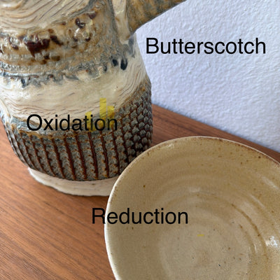 Two ceramic pieces labeled 'Butterscotch' and 'Oxidation' on a wooden surface.