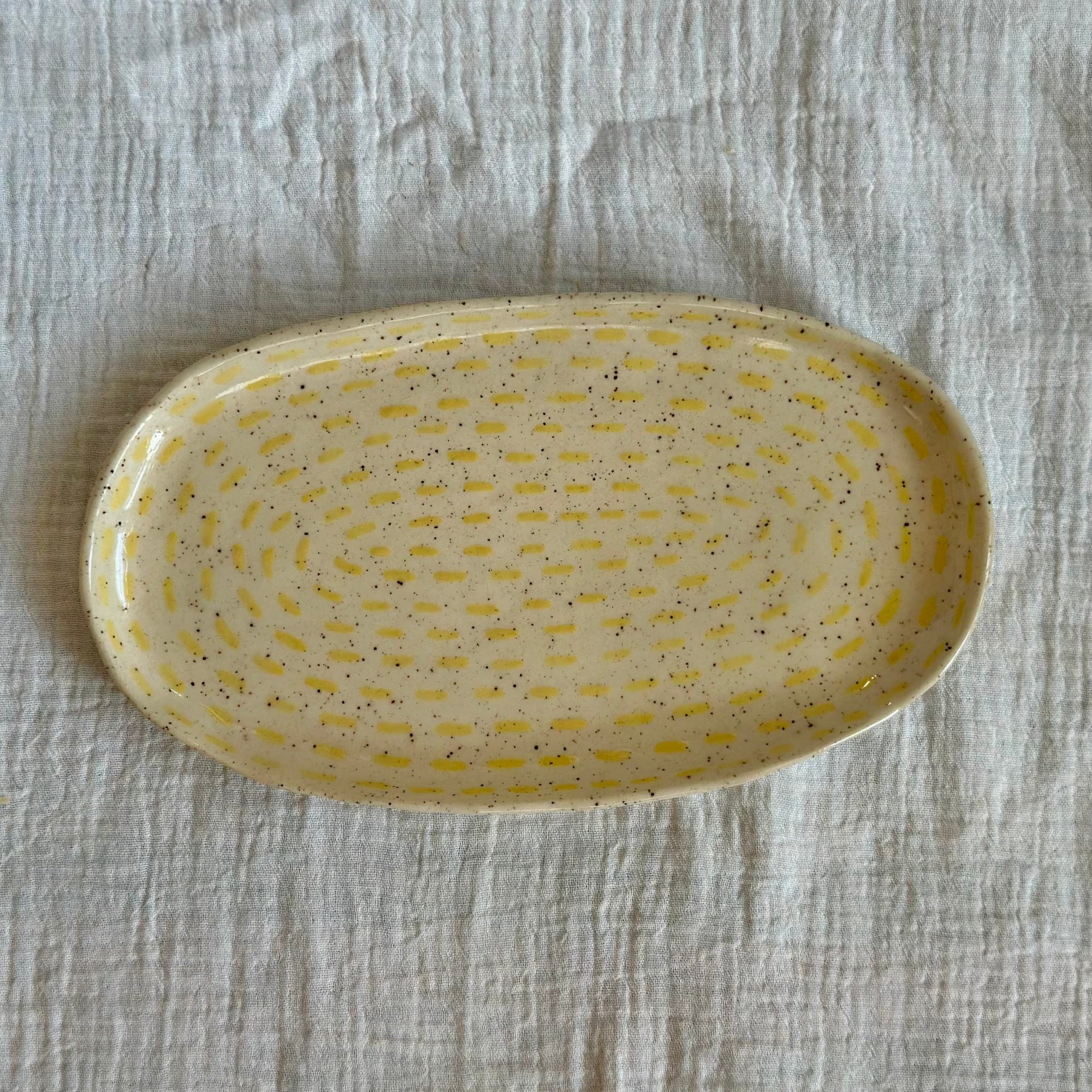 Yellow ceramic plate with speckled pattern on a textured gray surface