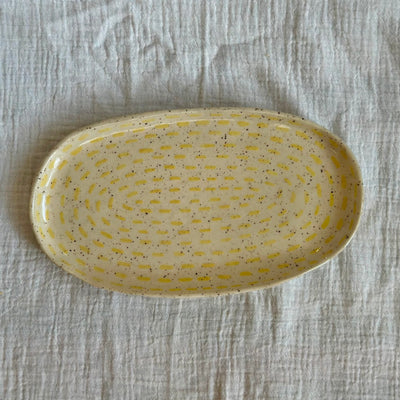 Yellow ceramic plate with speckled pattern on a textured gray surface