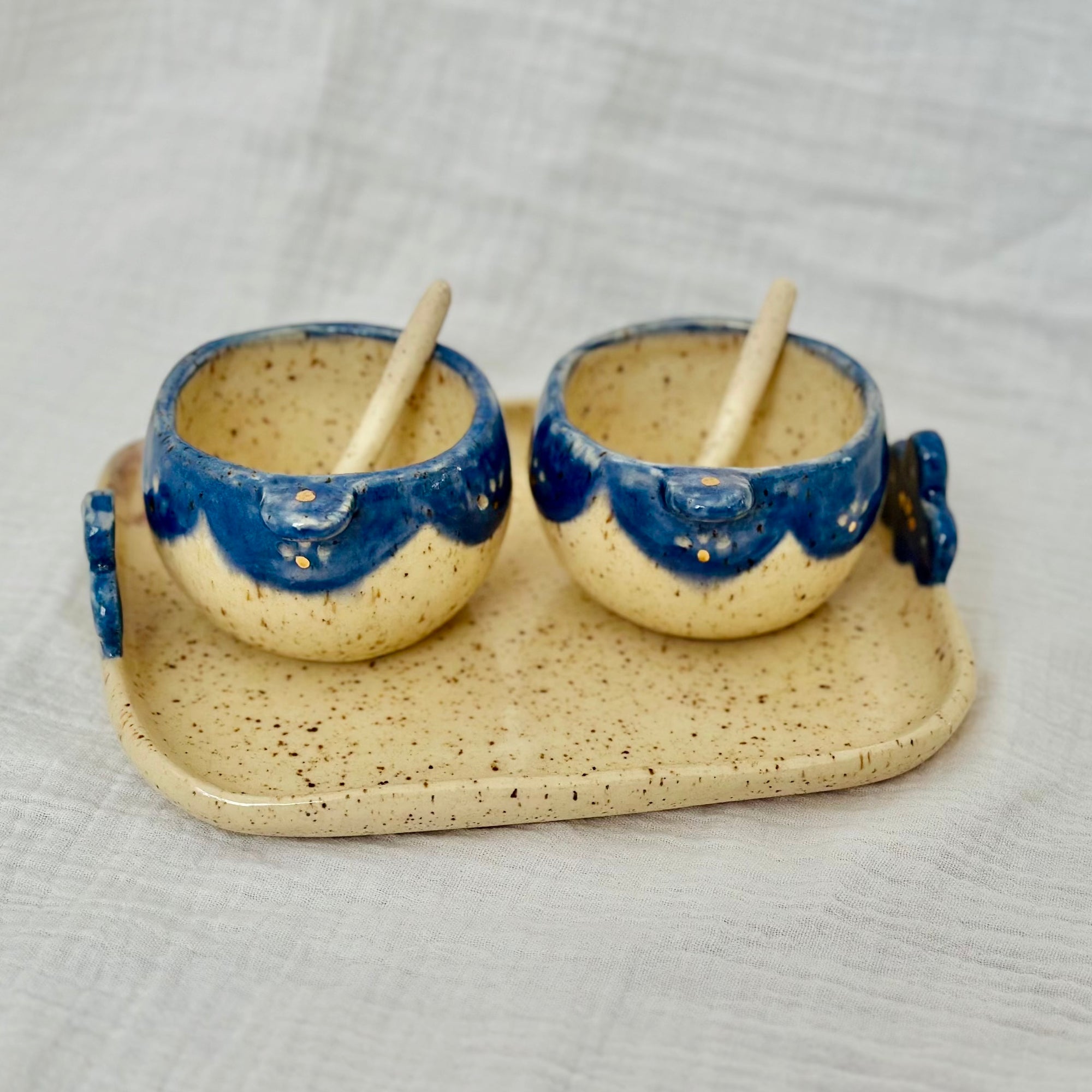 Pair of ceramic cups with blue rims on a matching tray against a light gray background
