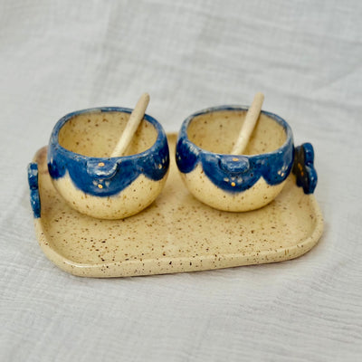 Pair of ceramic cups with blue rims on a matching tray against a light gray background